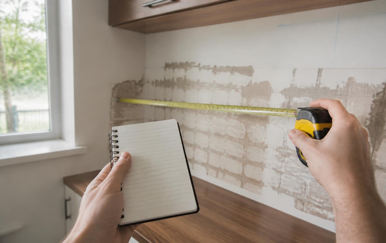 Hands measuring a kitchen wall with a tape measure before a renovation estimate